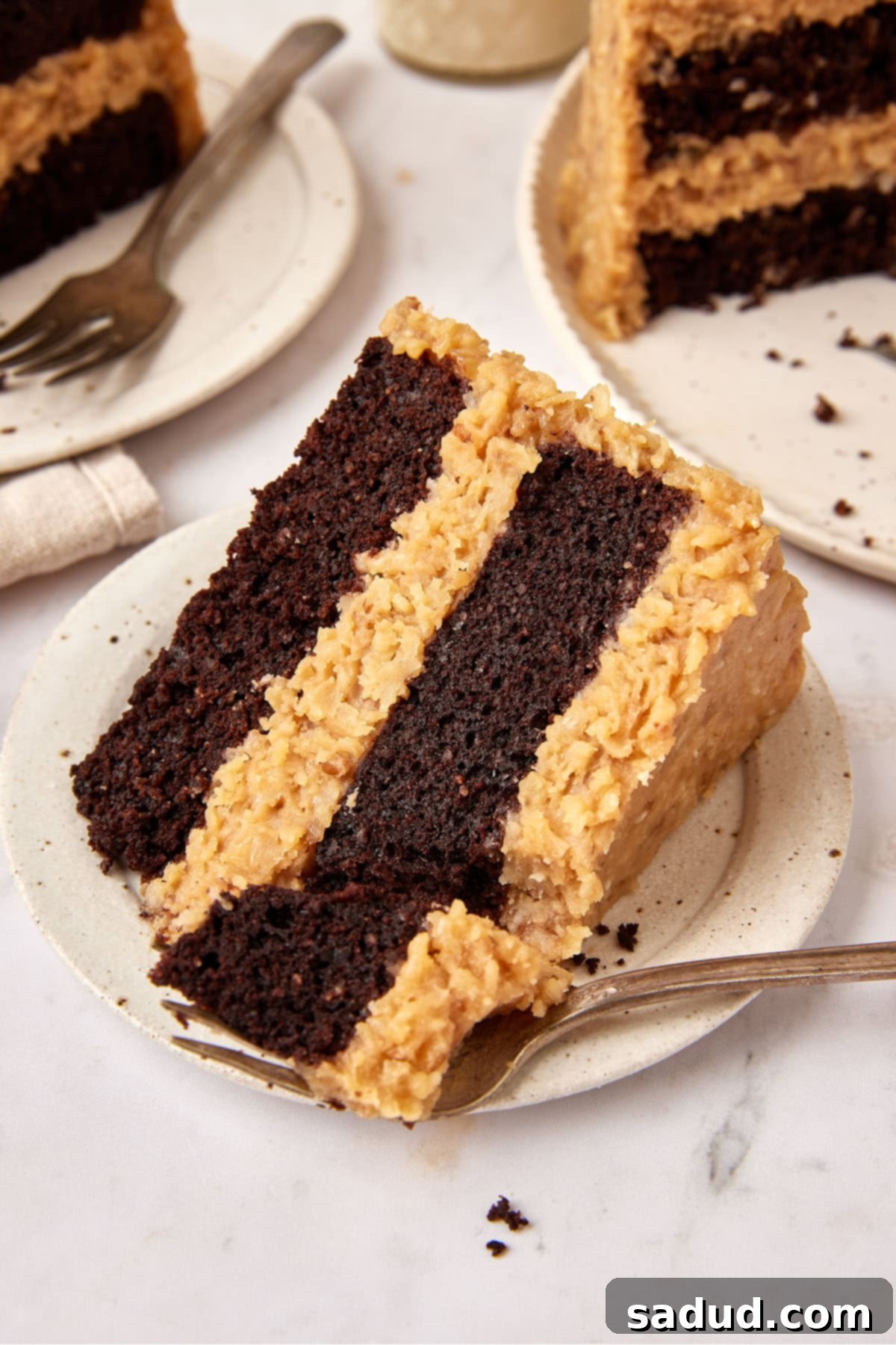 A plated slice of Keto German Chocolate Cake with a fork gently taking a piece from the thin edge of the wedge, highlighting the moist cake and fluffy frosting.