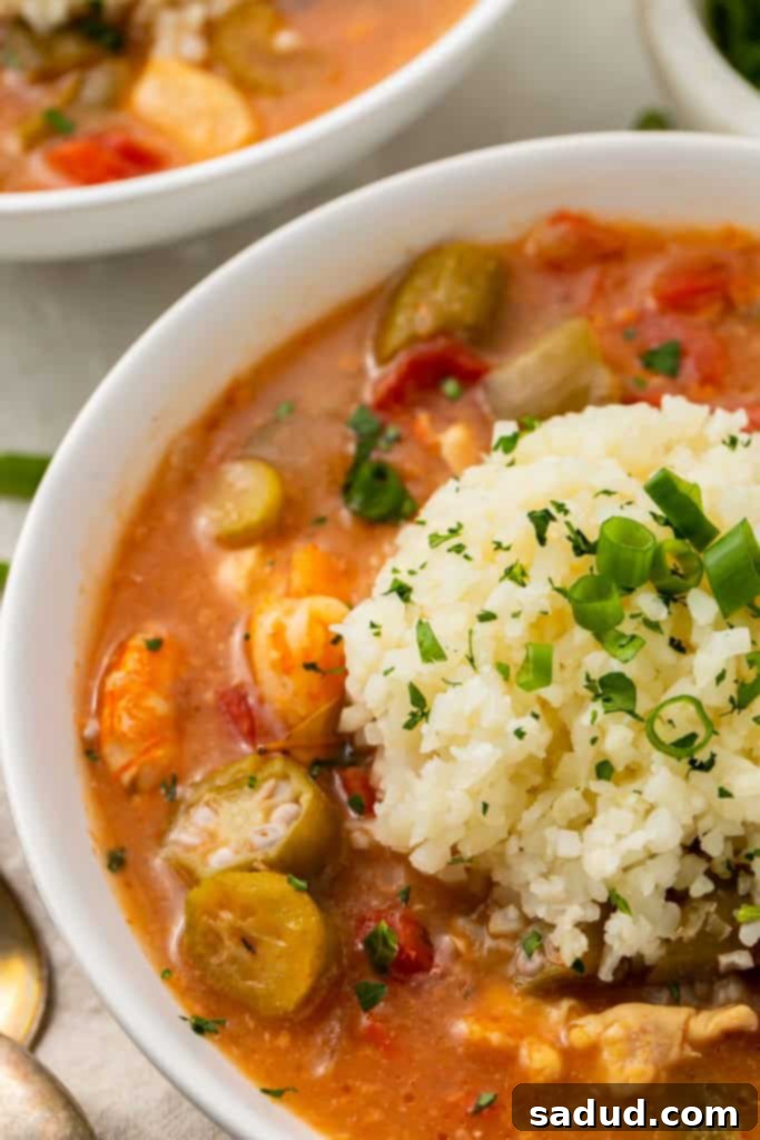 Close-up detailed photo of a white bowl of keto gumbo, showcasing the rich, thick broth, tender pieces of chicken, slices of andouille sausage, and vibrant shrimp.