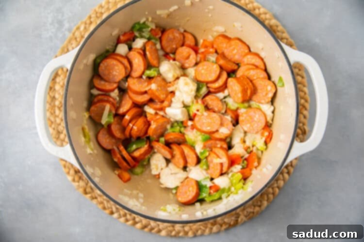 Sautéed vegetables and chicken with sliced andouille sausage, seasoned with thyme, salt, Cajun seasoning, and filé powder, in a large pot for gumbo base.