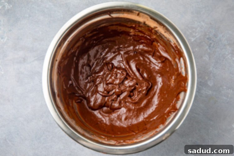 Smooth and rich chocolate mug cake batter in a large silver mixing bowl, ready for the mug.