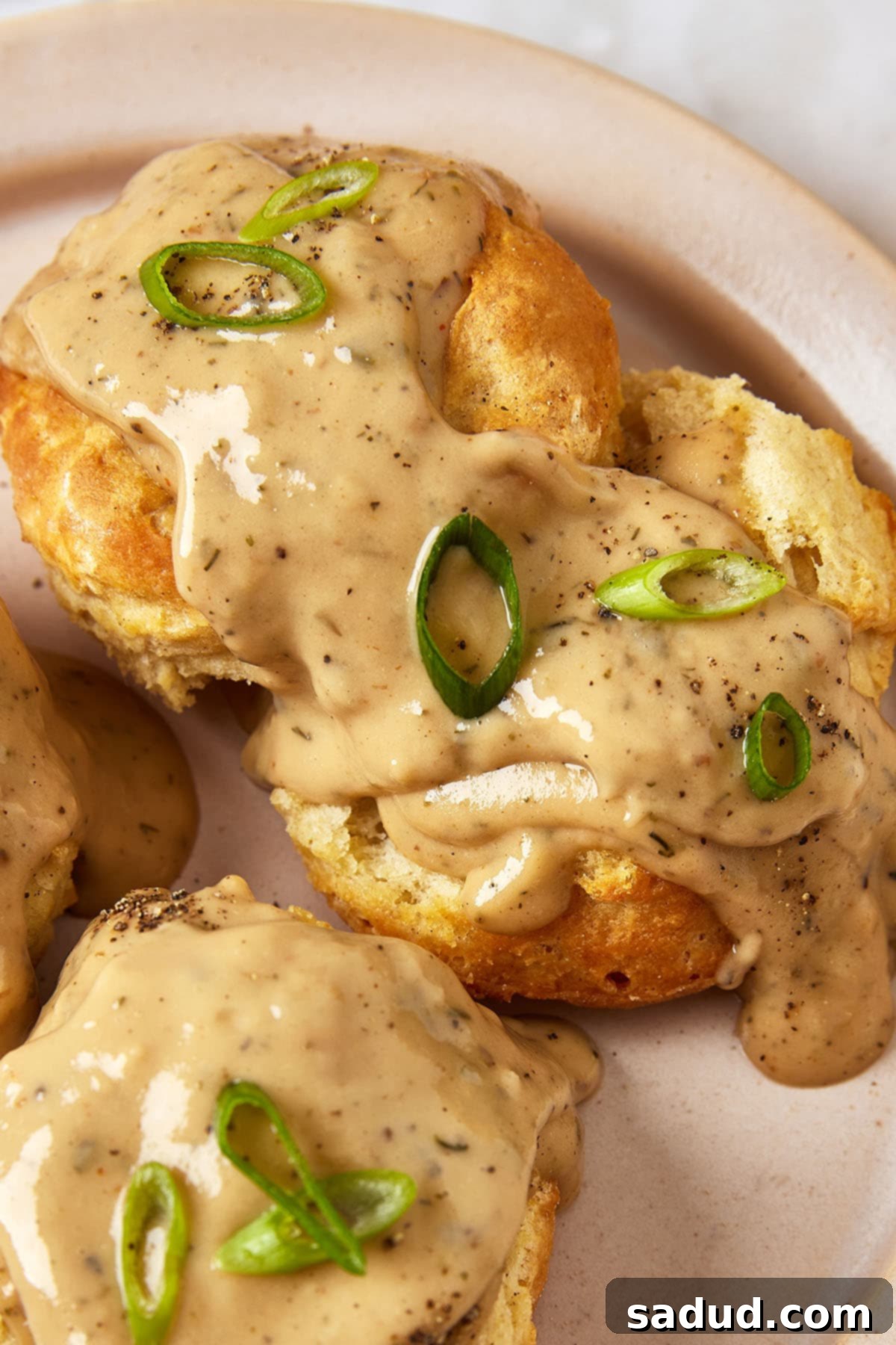 Vegan biscuits and gravy topped with sliced green onions on a plate, showcasing the fluffy biscuits and rich gravy.