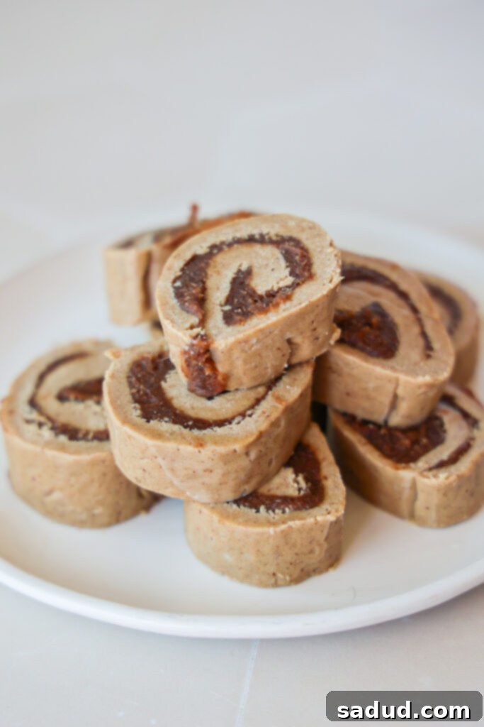 A log of raw vegan cinnamon roll dough being rolled with parchment paper, revealing the swirled cinnamon date filling and pecans.