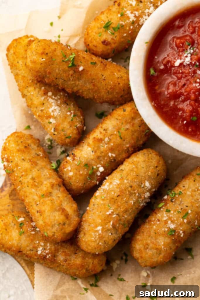 Frozen mozzarella sticks cooked in the air fryer then placed on a white plate with a small cup of marinara sauce