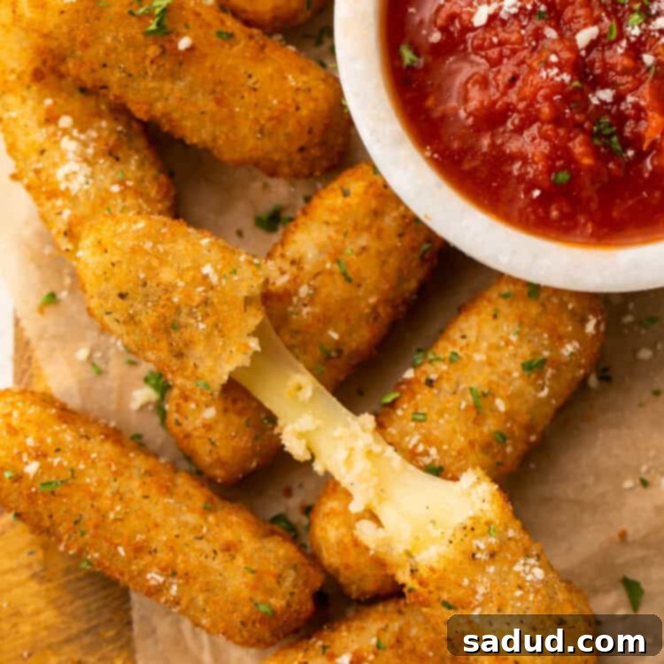 Frozen mozzarella sticks cooked in the air fryer then placed on a white plate with a small bowl of marinara