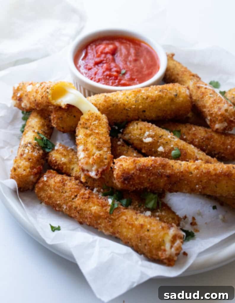 Golden-brown gluten-free mozzarella sticks neatly arranged on a white plate, served alongside a small ramekin of vibrant marinara sauce, ready to be enjoyed.