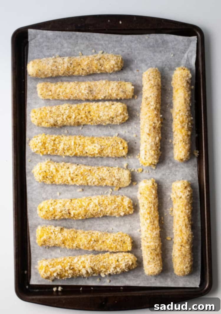 Gluten-free mozzarella sticks arranged on a baking sheet lined with parchment paper, ready for freezing.