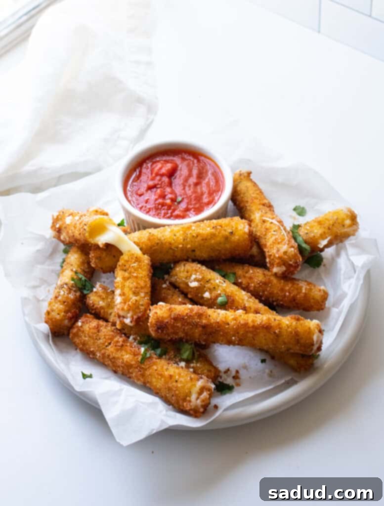 Close-up overhead view of golden gluten-free mozzarella sticks on a white plate, ready for dipping into a side of marinara sauce.