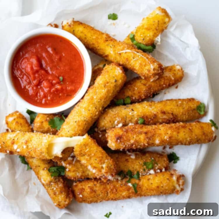 Overhead angle of gluten free mozzarella sticks on a white plate next to a ramekin of marinara sauce, garnished with fresh parsley.