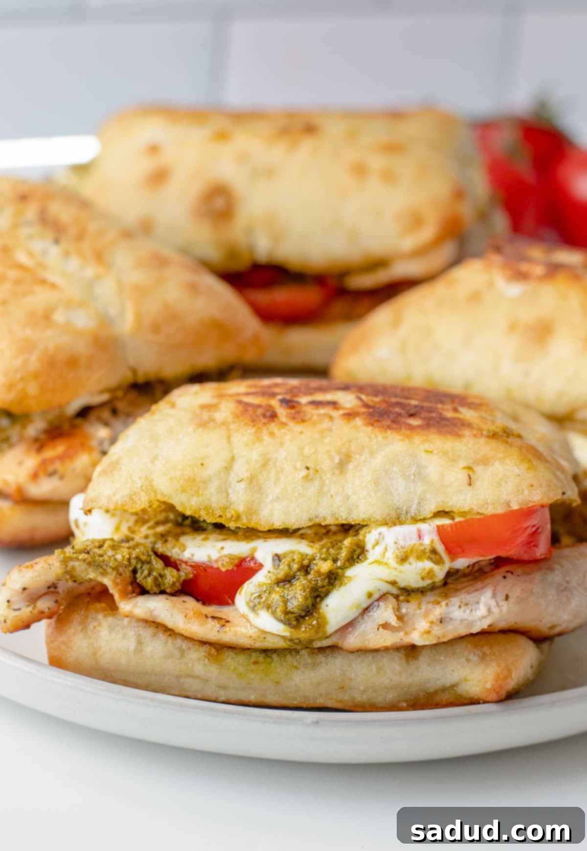 Zesty Pesto Chicken Sandwich 3 Side view of a chicken pesto sandwich on a plate with 3 other pesto sandwiches.