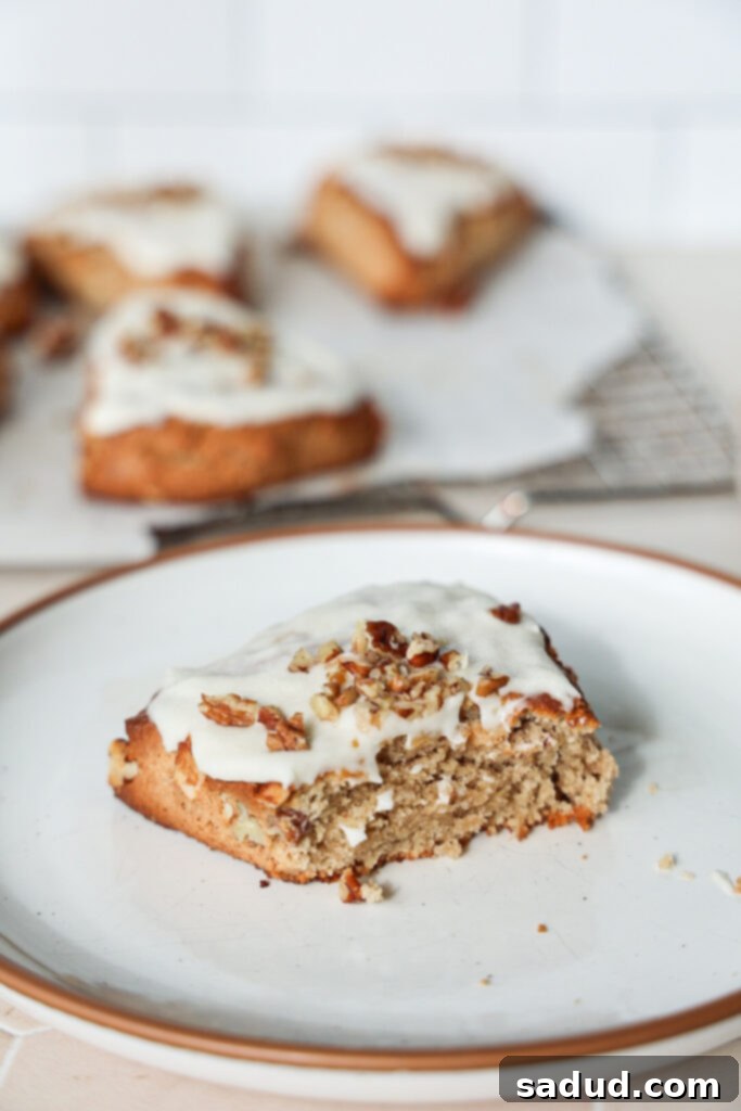 A single banana nut scone on a white plate, beautifully glazed with maple icing and sprinkled with chopped pecans.