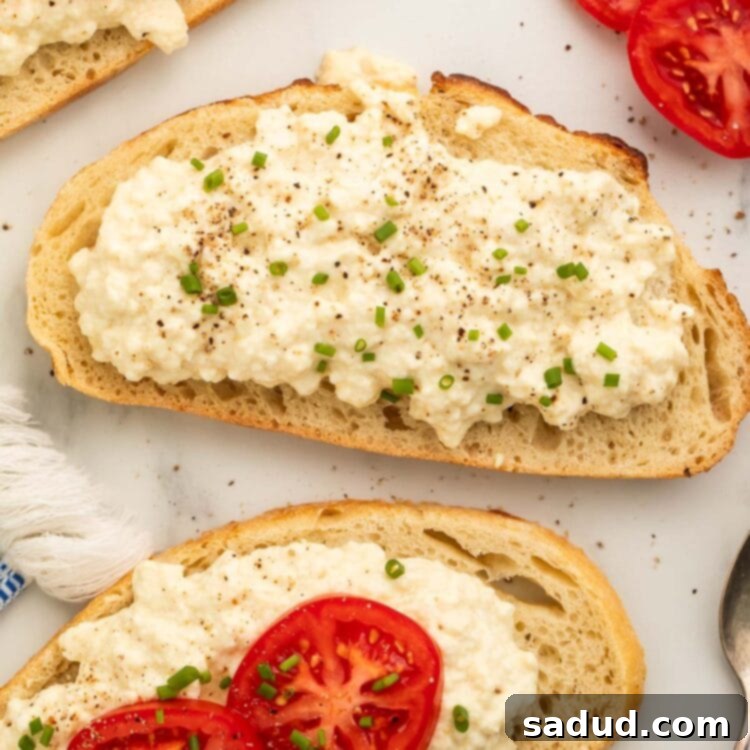 Homemade vegan cottage cheese spread on slices of French bread and topped with vibrant red tomato slices.