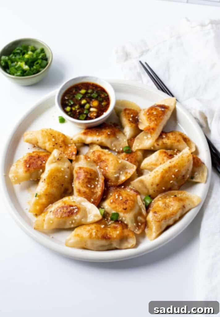 Chicken gyoza on a white plate with gyoza sauce and chopsticks, ready to eat.