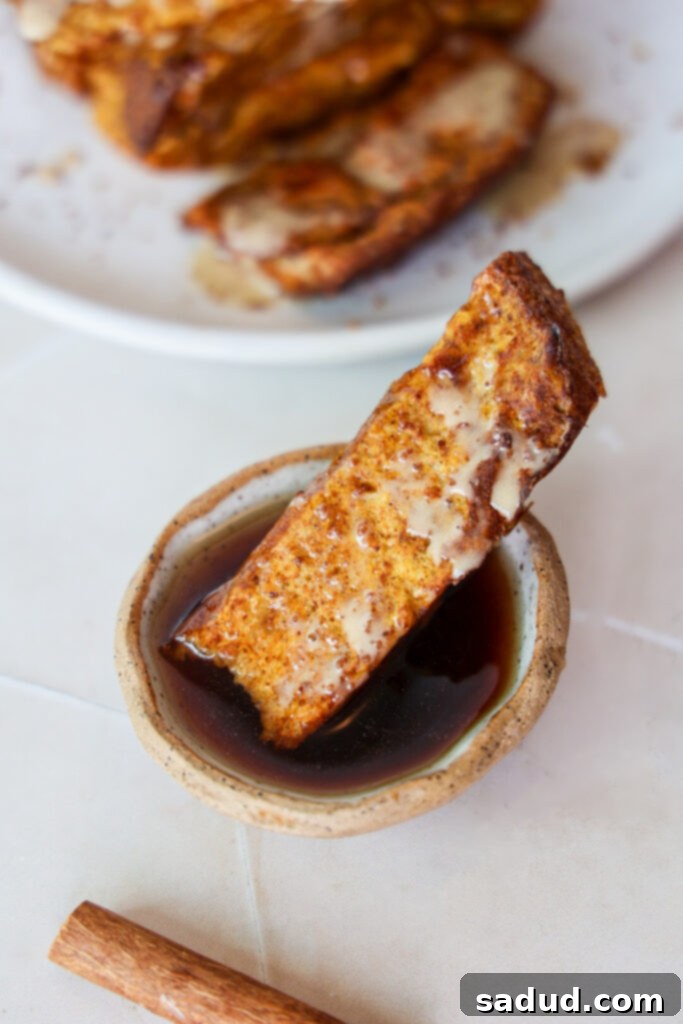 A single pumpkin spice french toast stick coated in maple syrup, held by a fork.