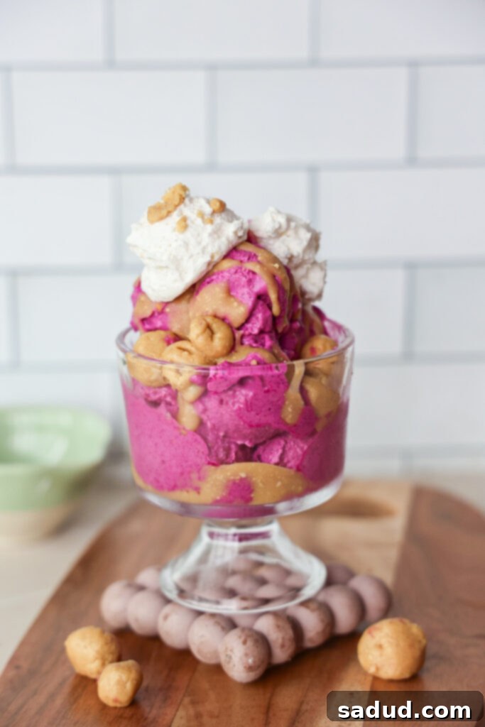 a bowl of dragonfruit ice cream with peanut butter magic shell and cookie dough pieces.