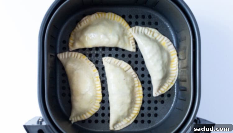 Unbaked empanadas in an air fryer basket