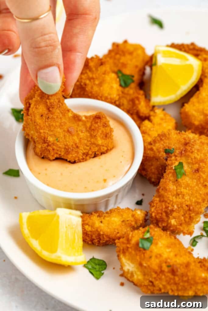 Crispy vegan shrimp being dipped into a bowl of sriracha mayo, showing its golden-brown texture.
