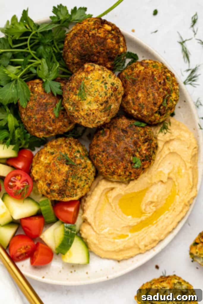 Air fryer falafel on a plate with hummus, cucumbers, tomatoes, fresh parsley, and dill, showcasing a delicious meal.
