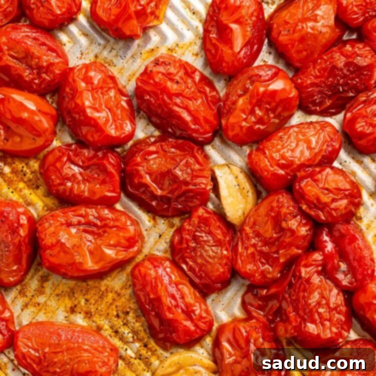 Wrinkled, roasted grape tomatoes and garlic cloves on a silver baking sheet.