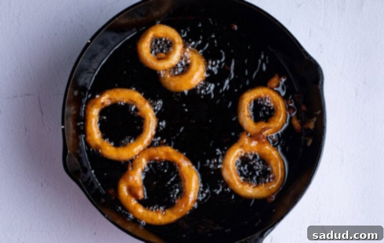 Gluten free onion rings frying in oil in a large cast iron skillet