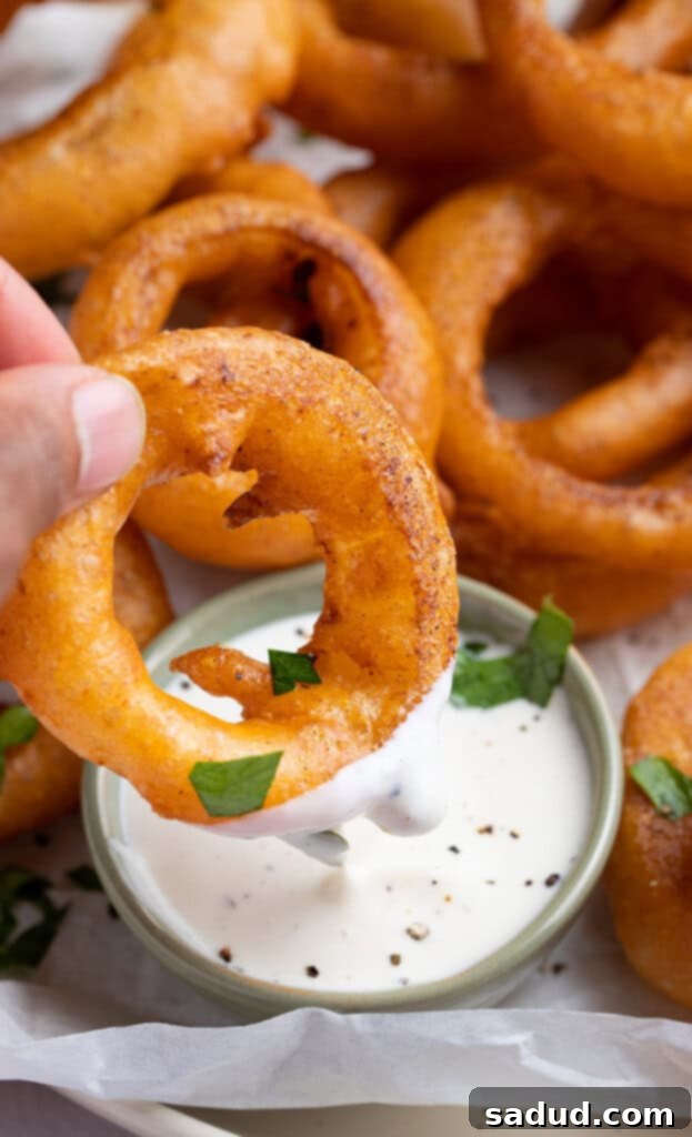 Crispy Gluten-Free Onion Rings 3 Individual onion ring being dipped into ranch dressing, with more onion rings out of focus in the background