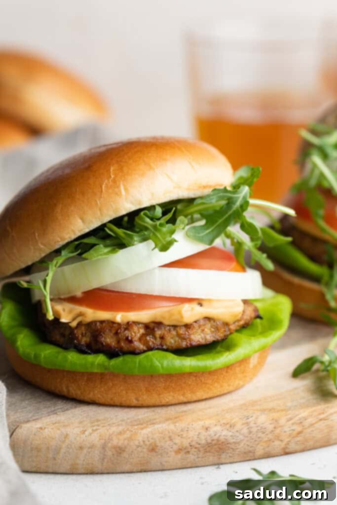 Close-up of a perfectly cooked air fryer turkey burger, garnished with crisp lettuce, ripe tomato, red onion, a generous dollop of chipotle mayo, and fresh arugula, showcasing its delicious layers and vibrant colors.