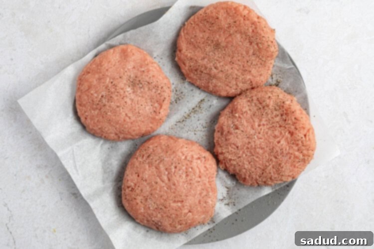 Pre-made turkey burger patties are being seasoned with salt and black pepper, ready for air frying.