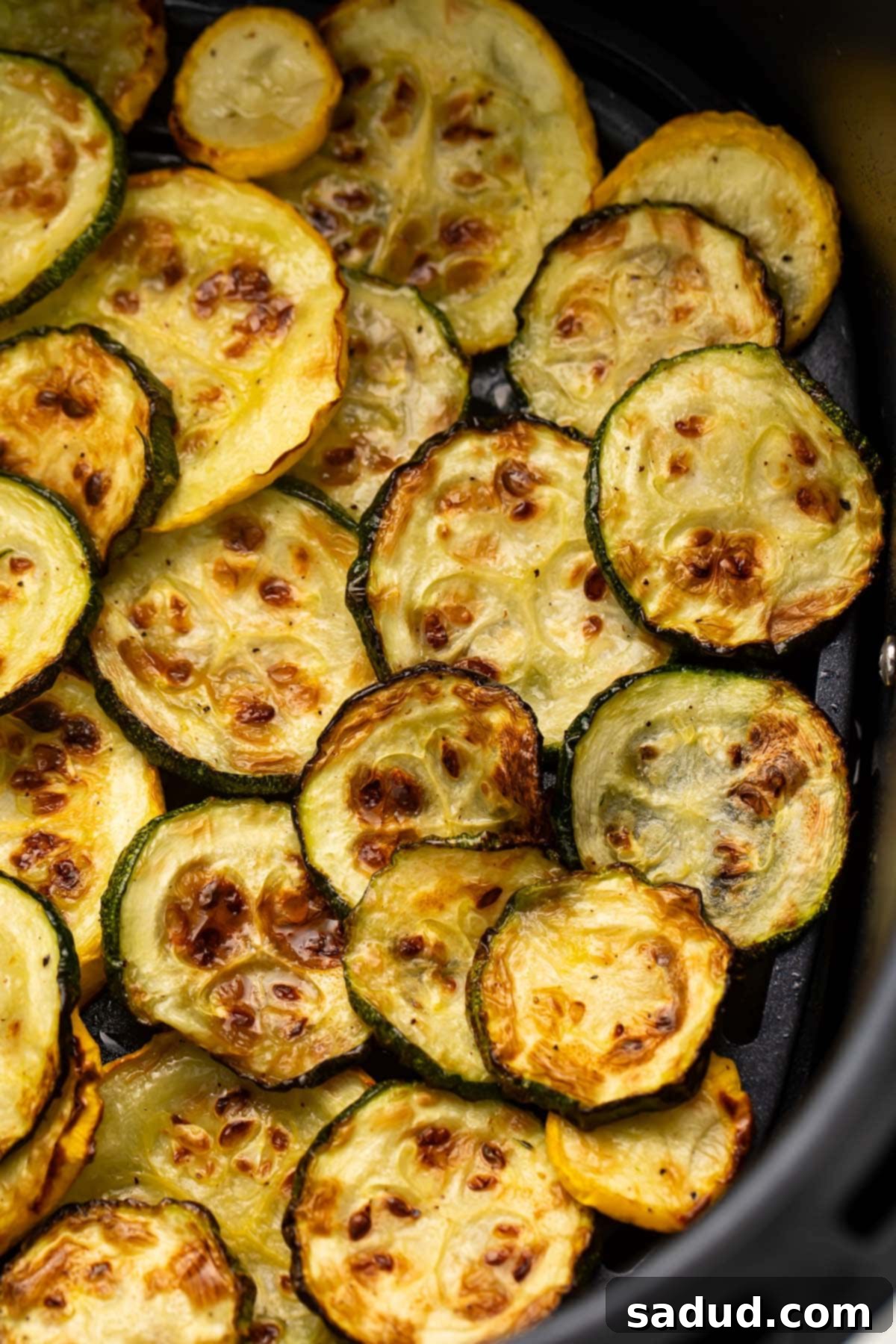 Several discs of vibrant yellow and green squash laid out neatly in an air fryer basket, ready for cooking to achieve perfect crispiness.