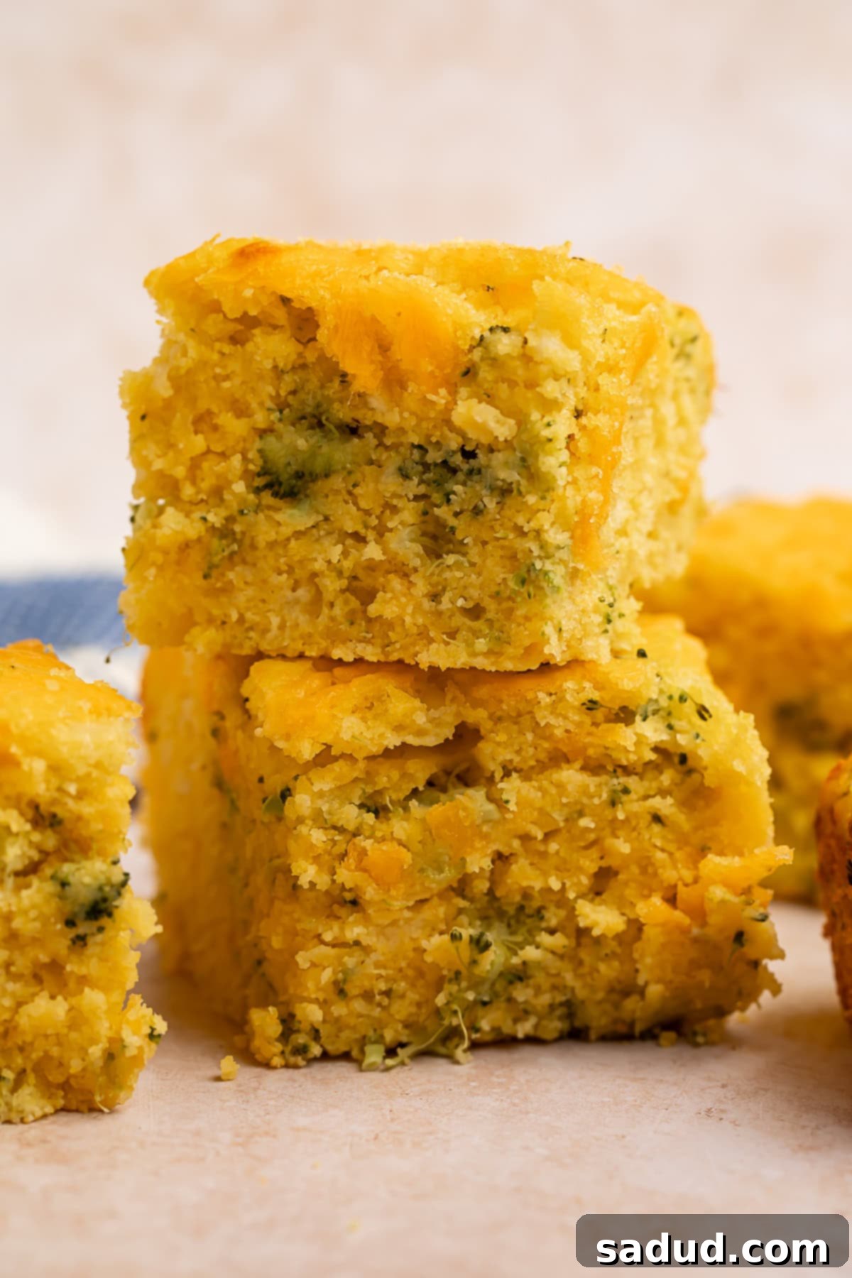 Two golden-brown squares of cheesy broccoli cornbread, stacked one on top of the other, showcasing its moist texture and green flecks.