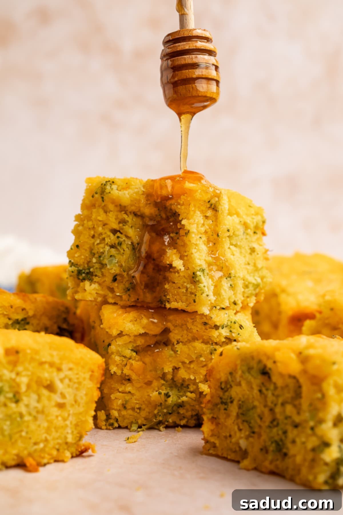 A stream of golden honey being drizzled over two perfectly baked squares of broccoli cornbread, adding a touch of sweetness.