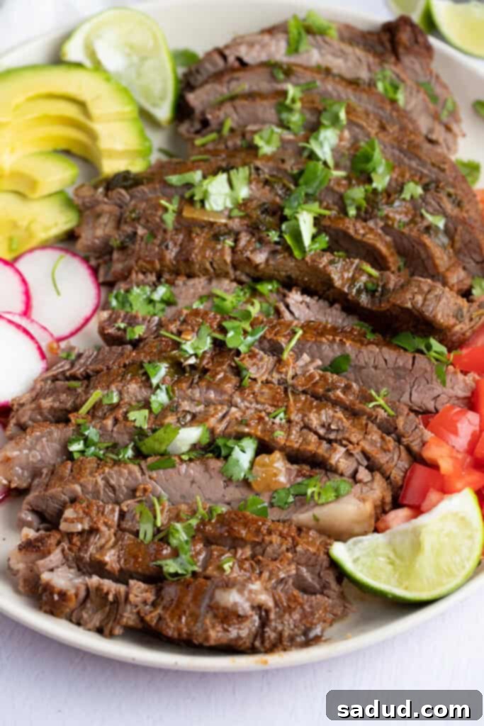 Sliced Instant Pot carne asada on a white plate surrounded by vegetables