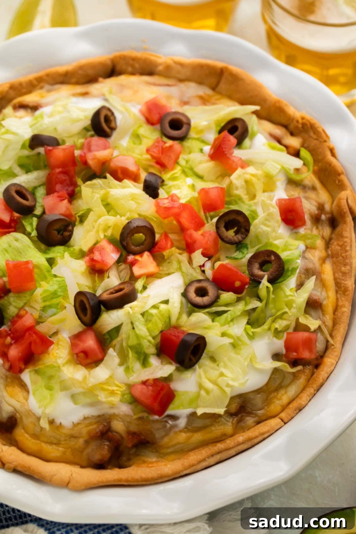 Close-up of taco pie in a white ceramic pie plate on a table, showing the golden-brown crust and melted cheese topping.
