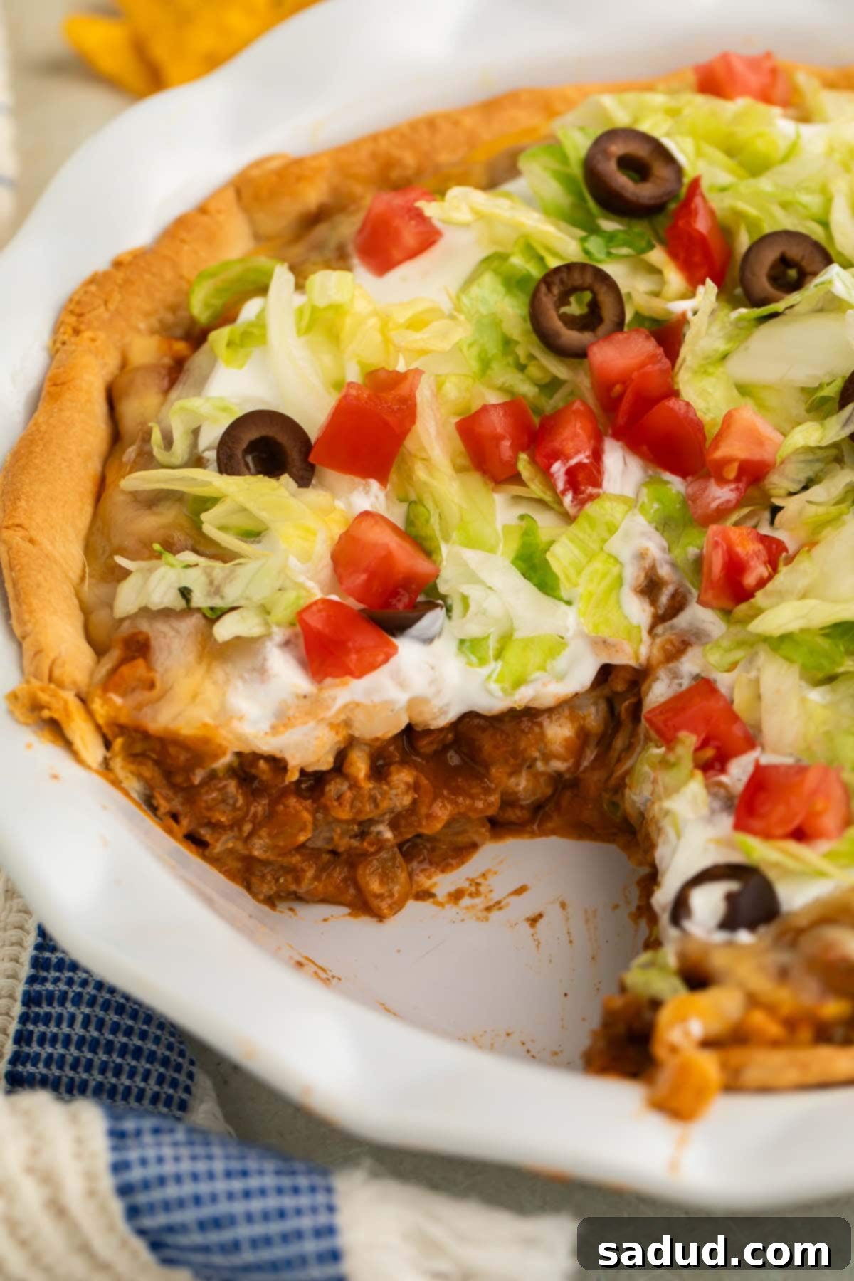 Side view of a crisp taco pie topped with shredded lettuce and diced tomatoes in a white pie dish.