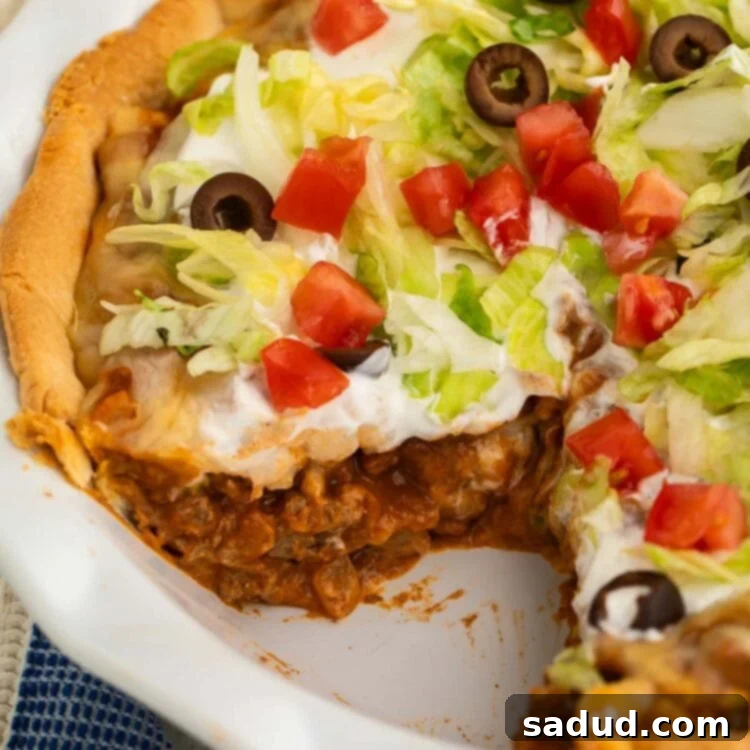 Side view of a crisp taco pie topped with shredded lettuce and diced tomatoes in a white pie dish.