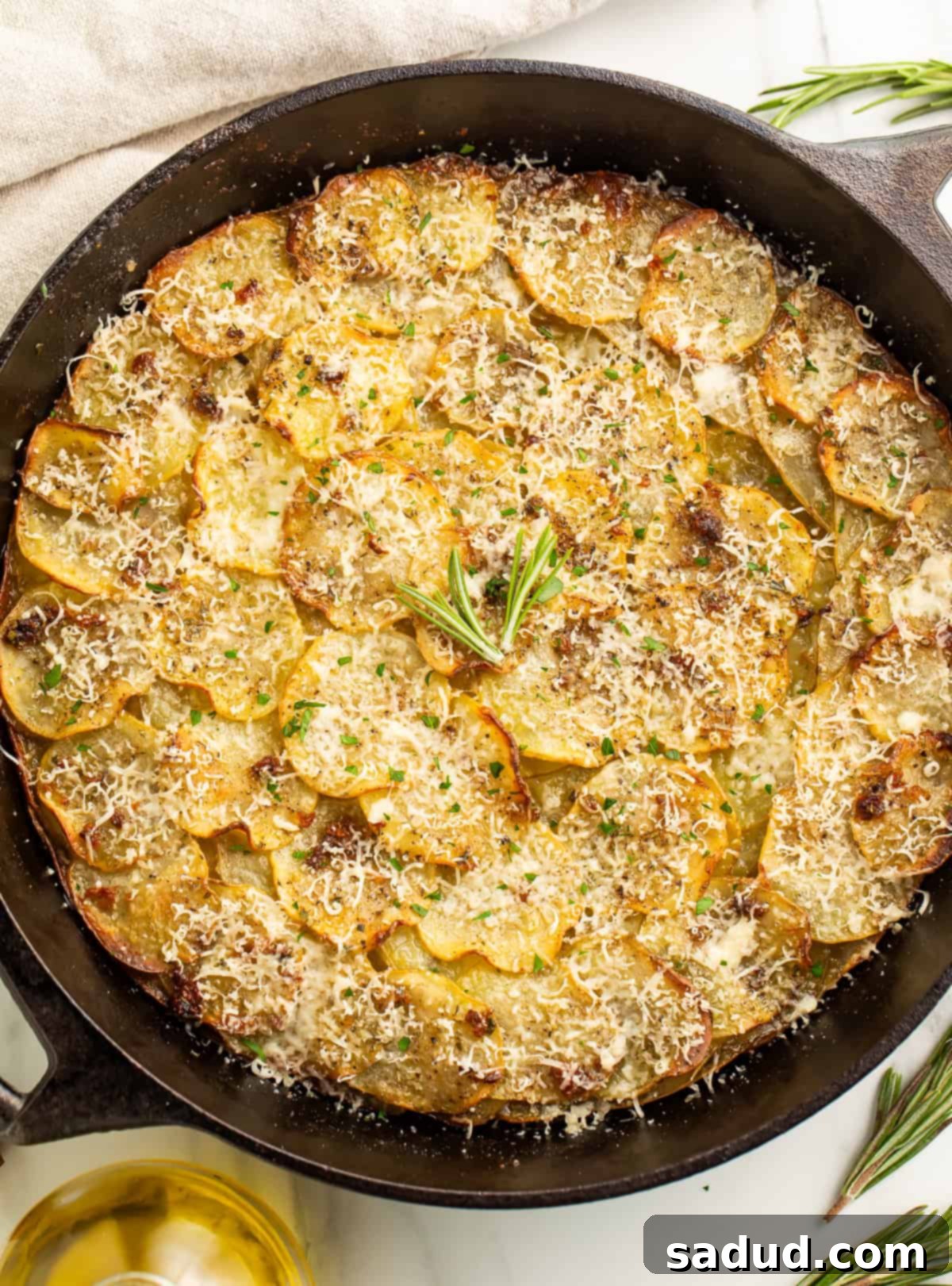 Overhead image of a potato galette in a cast iron skillet, golden brown and garnished with fresh rosemary.