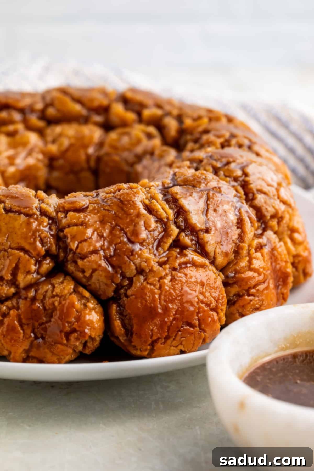 Side on view of monkey bread on a white plate with a white bowl of caramel off to one side.