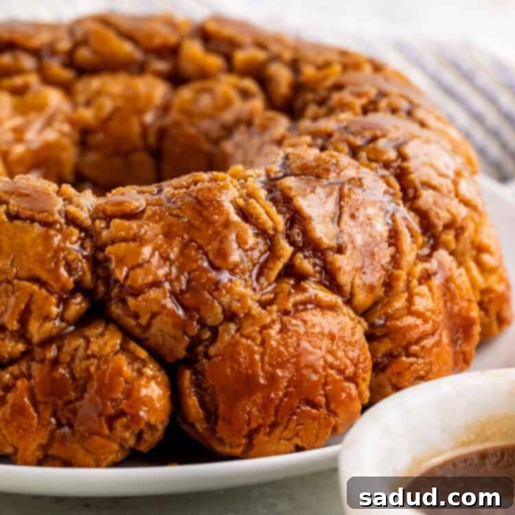 Side on view of monkey bread on a white plate with a white bowl of caramel off to one side.