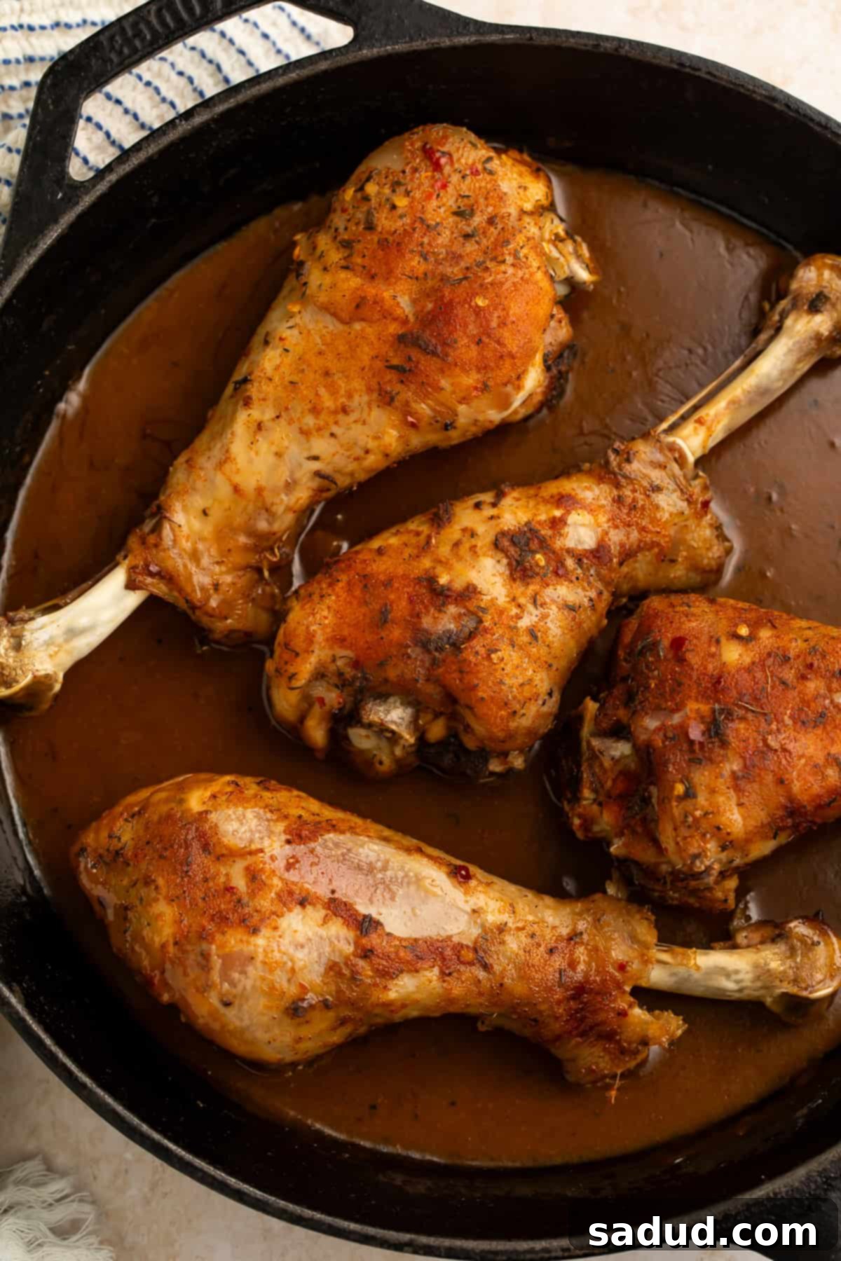 Succulent Oven-Roasted Turkey Drumsticks 4 Close up of four perfectly roasted turkey legs in a cast iron skillet of dark brown gravy, showcasing the crispy skin.