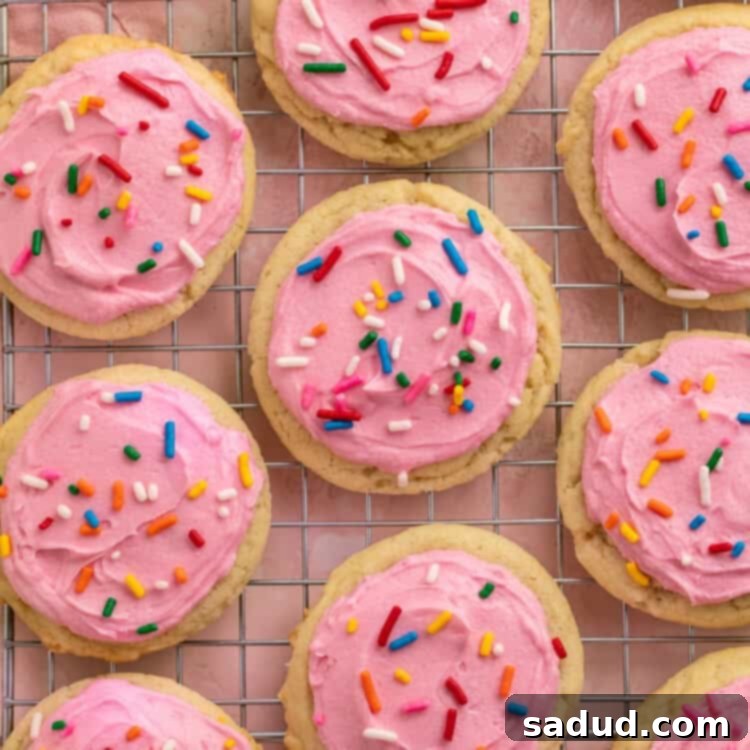 Pink frosted sugar cookies with rainbow sprinkles on a cooling rack.