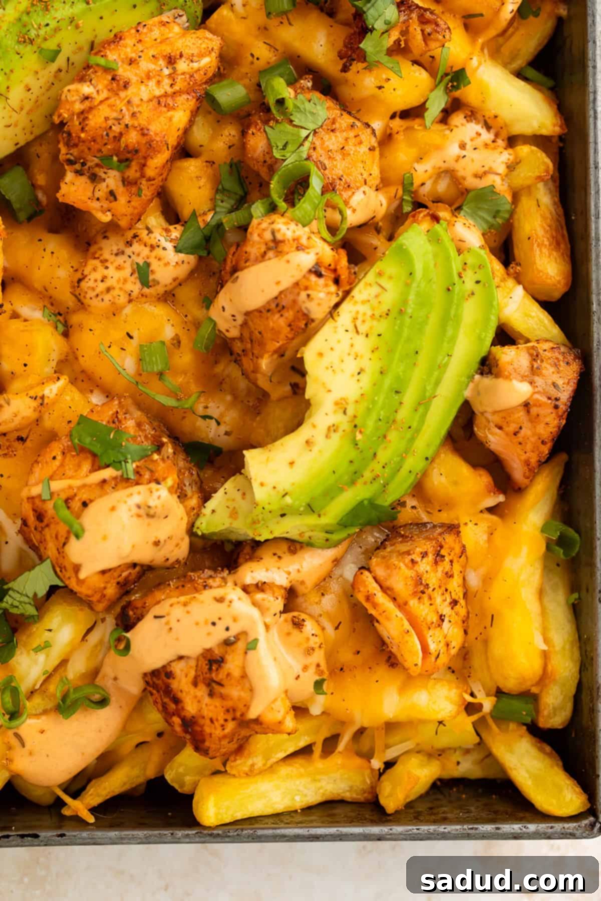 Close up of sliced avocado, Cajun salmon pieces and French fries in a metal tray. 