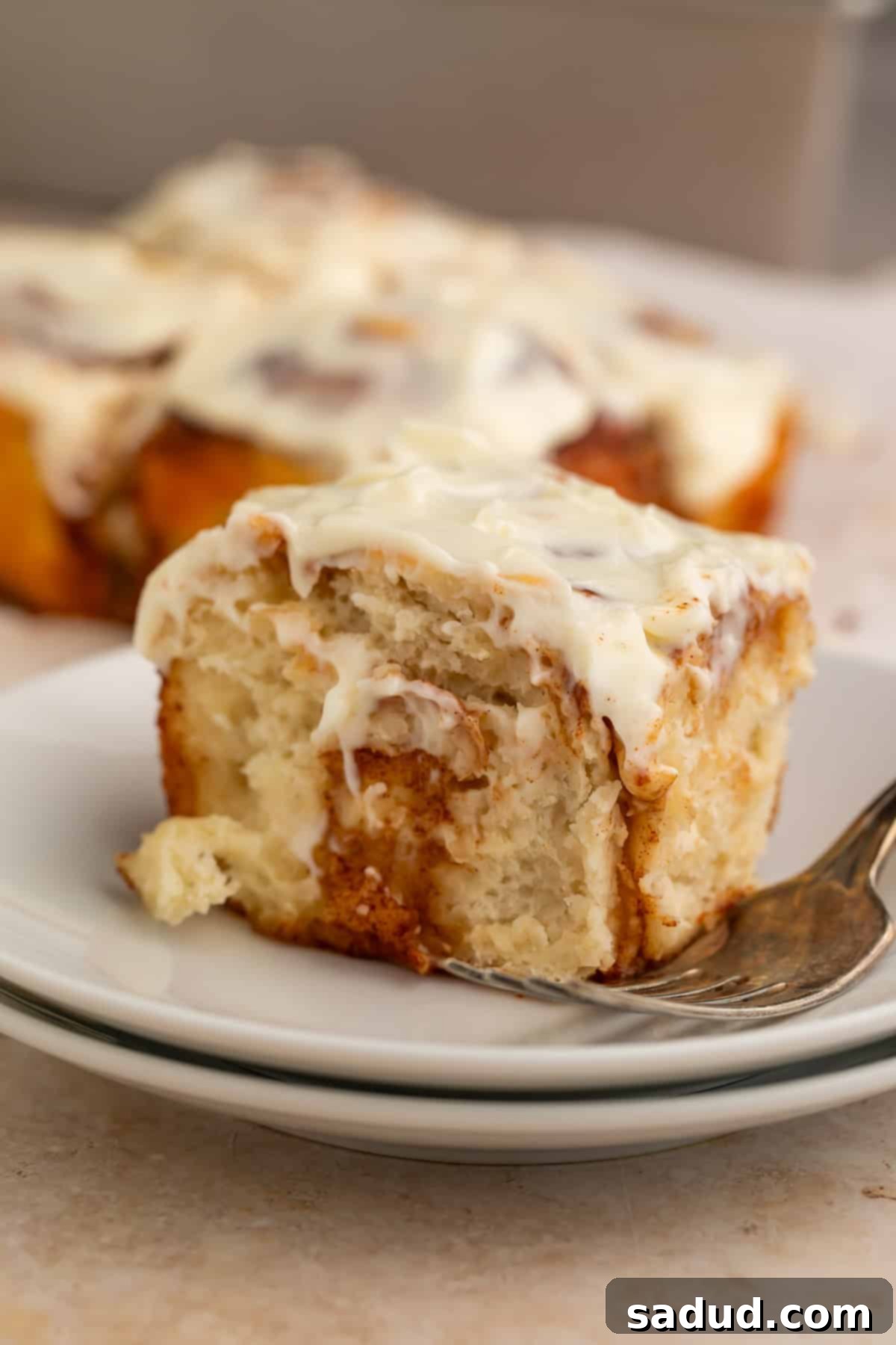 Frosted cinnamon roll on a stack of white plates with a fork.