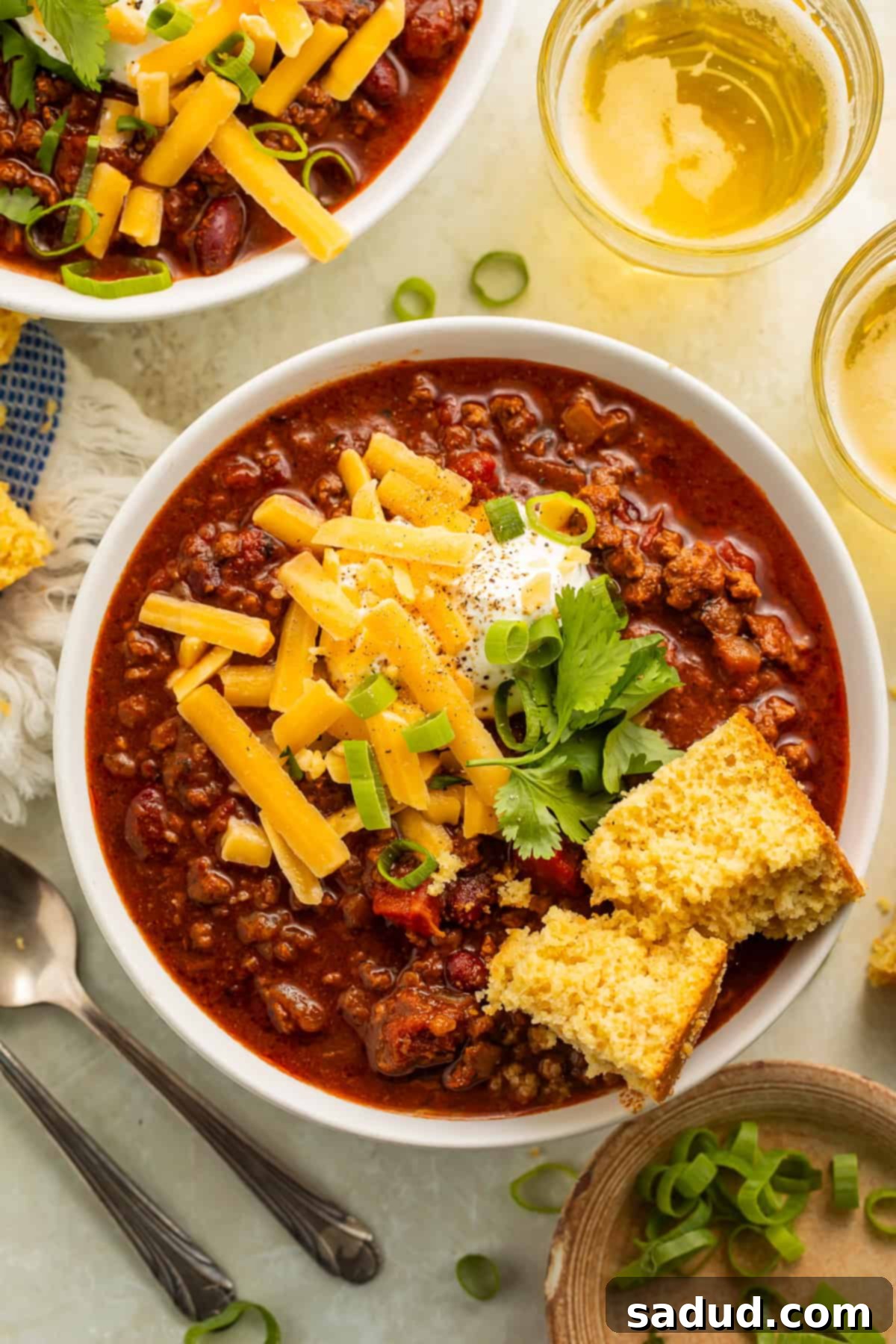 A close-up shot of a bowl of gluten-free chili topped with cornbread, green onions, sour cream, and shredded cheese, highlighting the delicious toppings and textures.