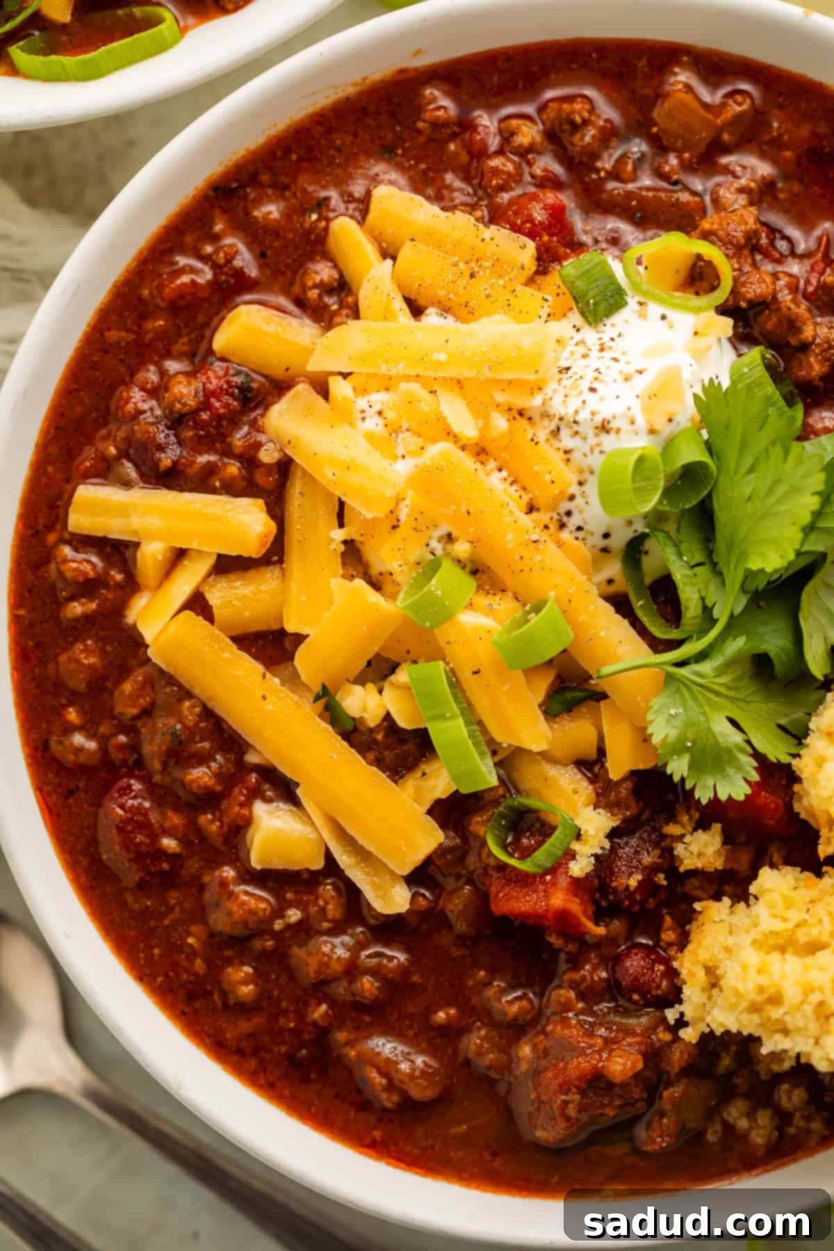 An even closer shot of the chili, showcasing the individual ingredients like beans and ground meat, along with the colorful toppings of shredded cheese, sour cream, green onions, and cilantro.