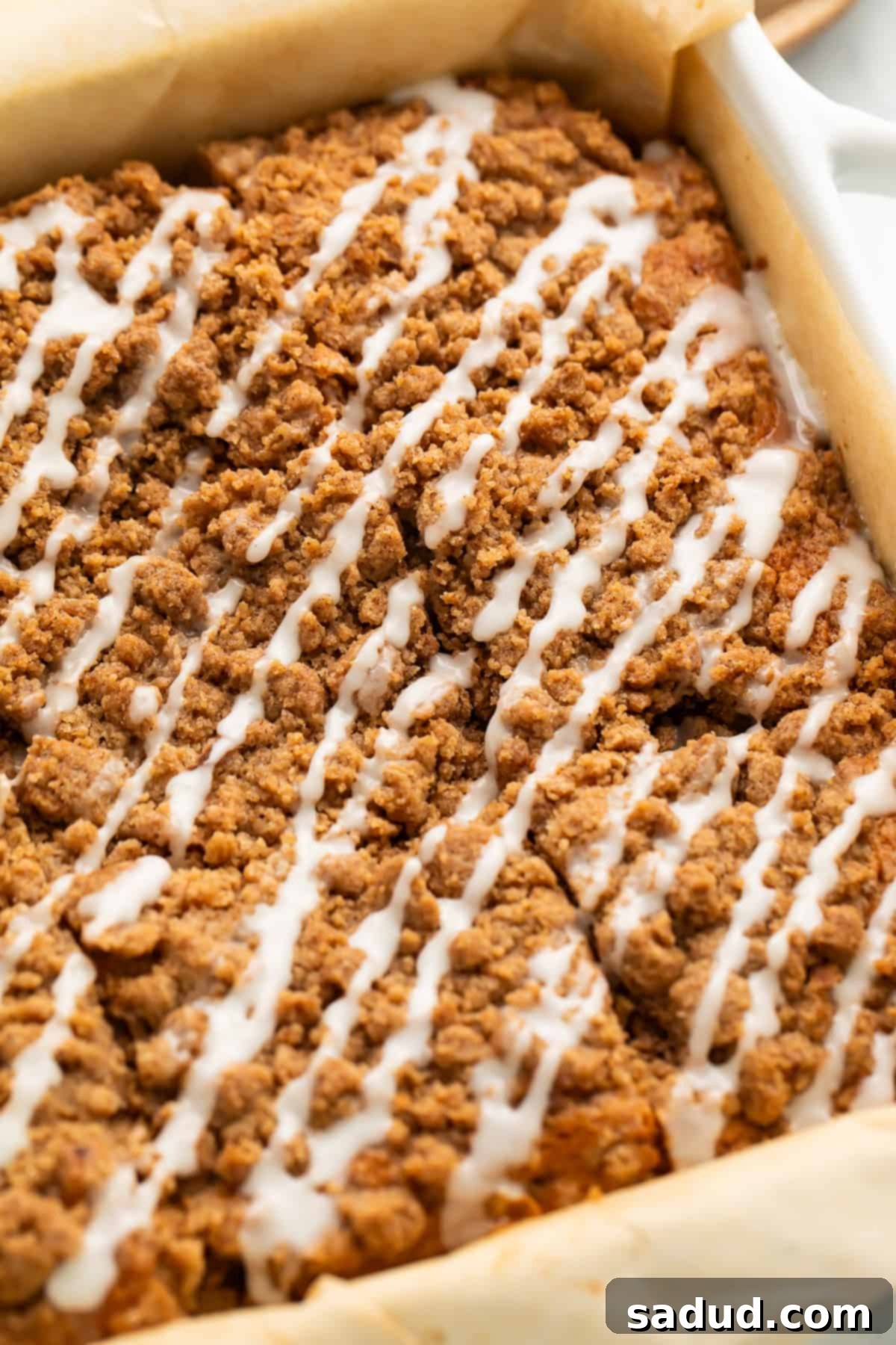 Gluten-Free Coffee Cake Bliss 3 Coffee cake with a streusel topping and iced drizzle cut into squares inside a parchment-lined pan.