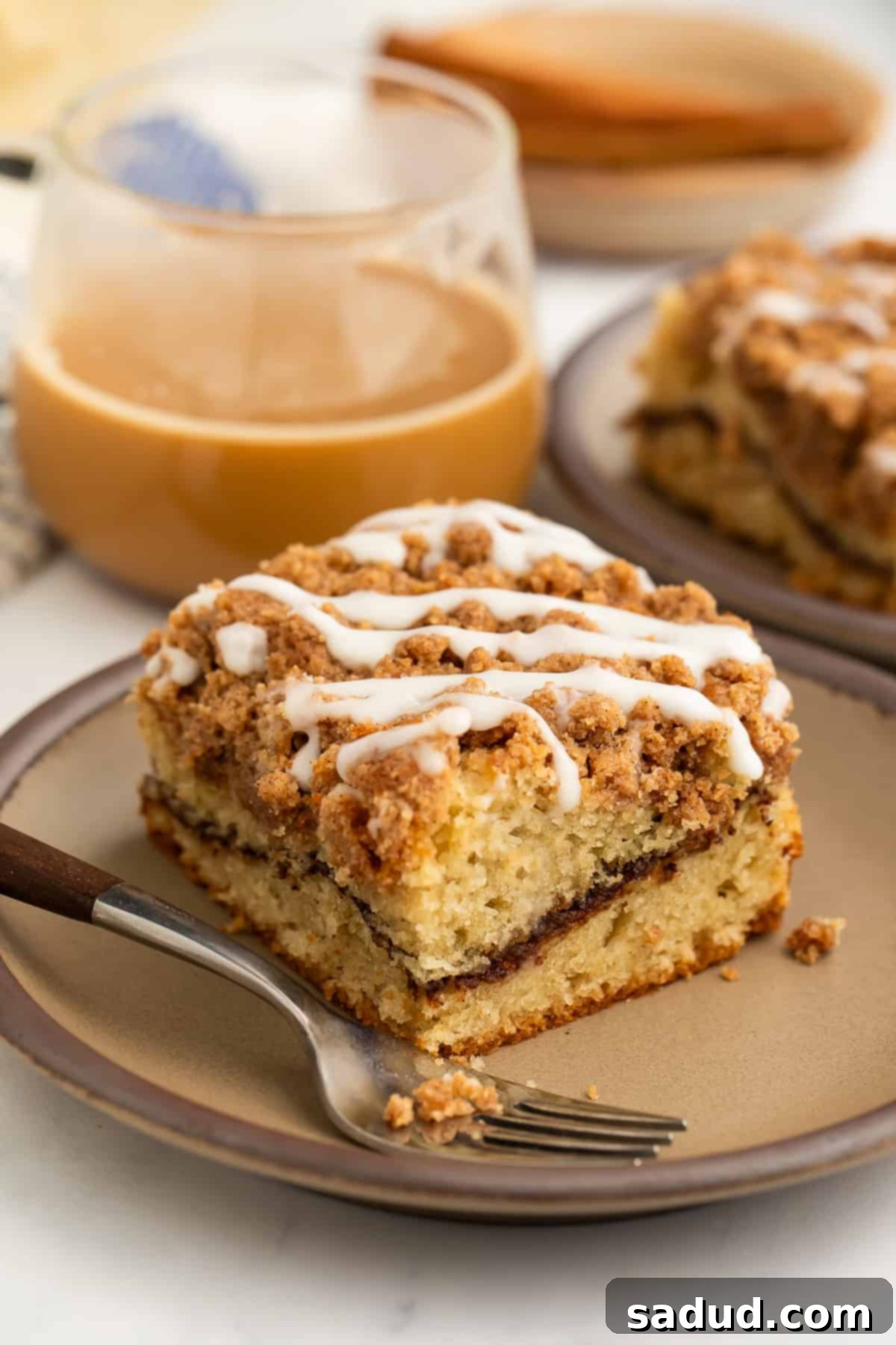 Gluten-Free Coffee Cake Bliss 4 Slice of gluten free coffee cake with streusel topping on a plate with a fork and an iced coffee in the background.